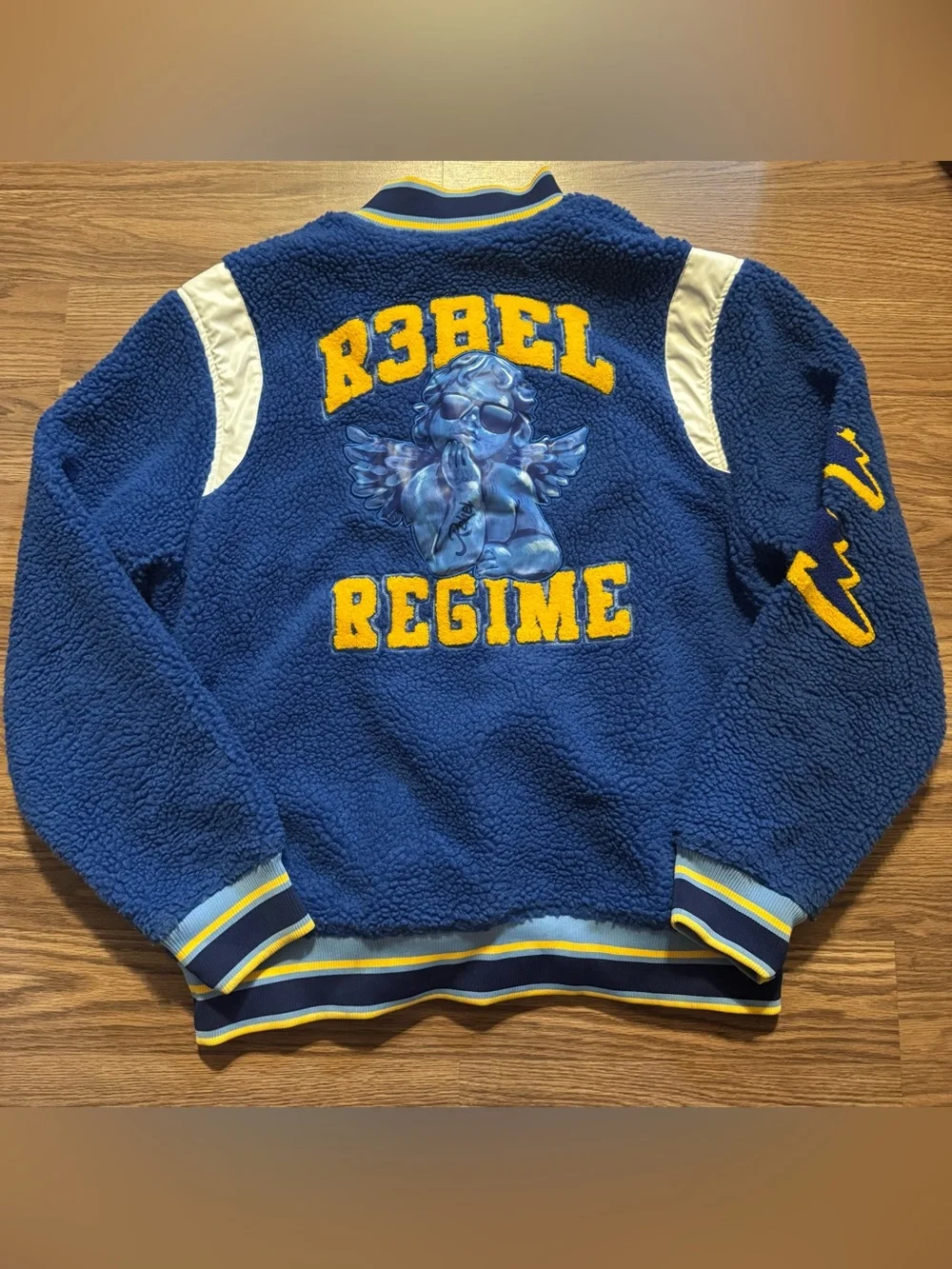 Soft  blue sherpa jacket with bold yellow 'Rebel Regime' lettering and angel